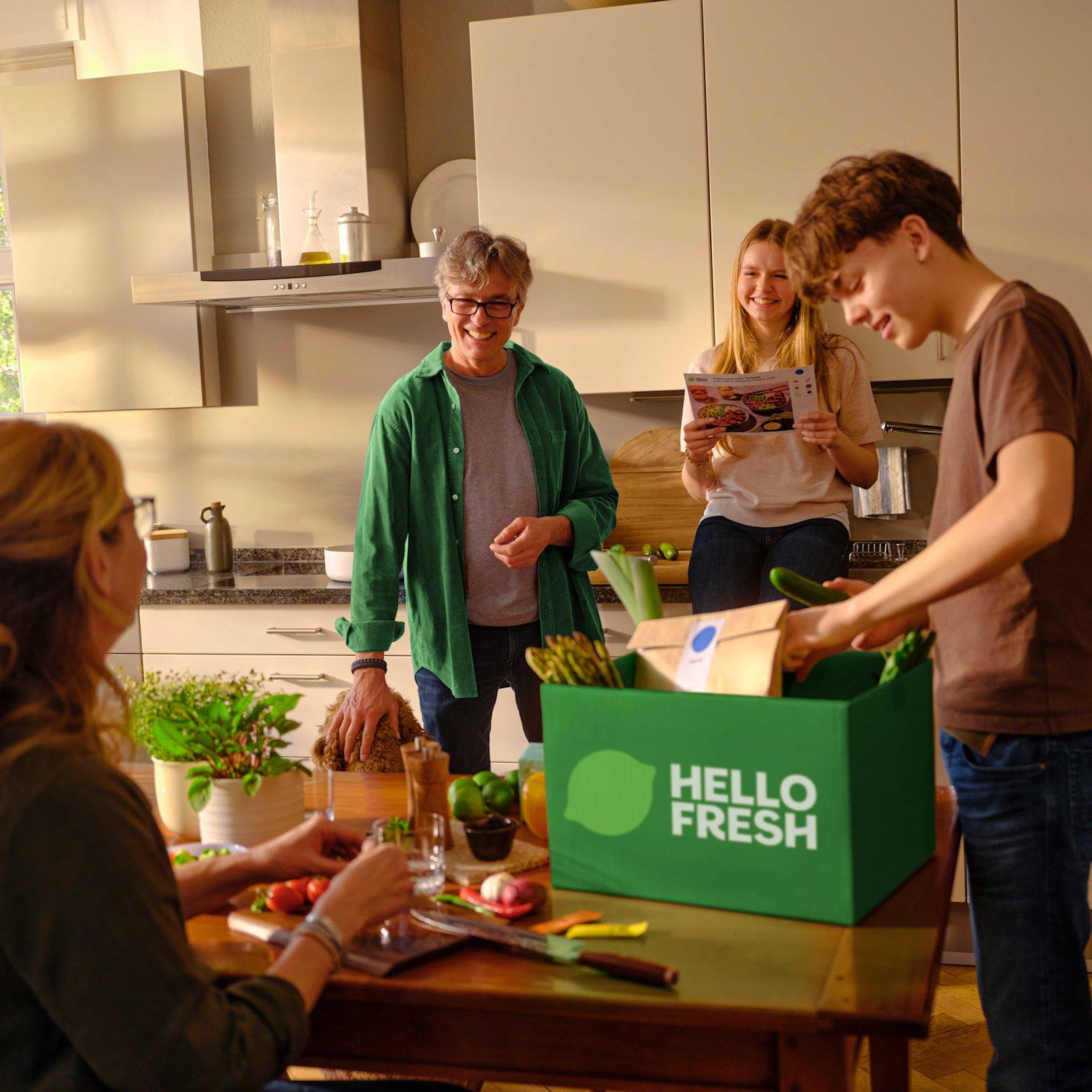 Familie pakker ut en HelloFresh-kasse på kjøkkenet og leser oppskriftskortet